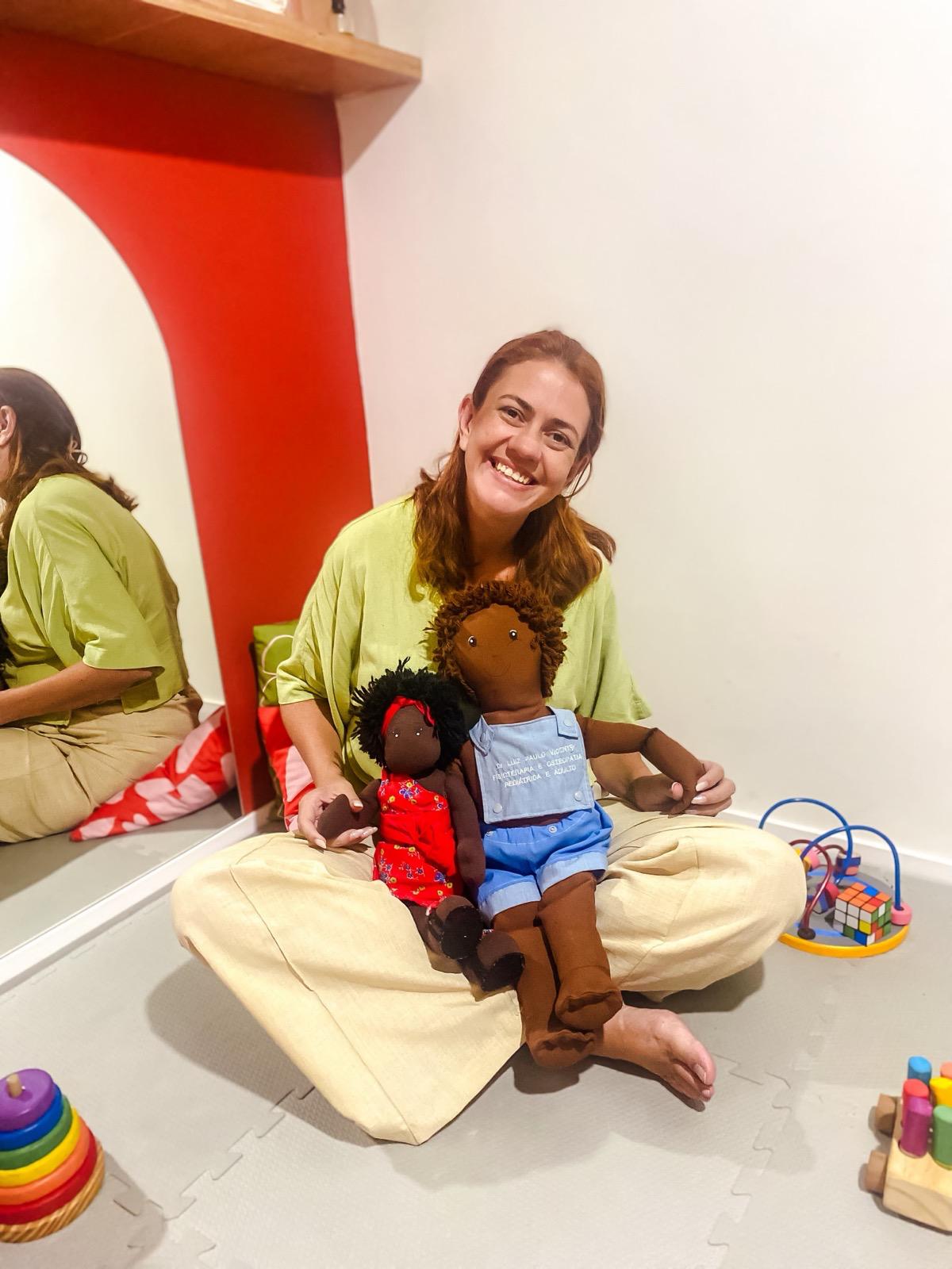 Dra. Karla sentada no chão com bonecos usados nas consultas